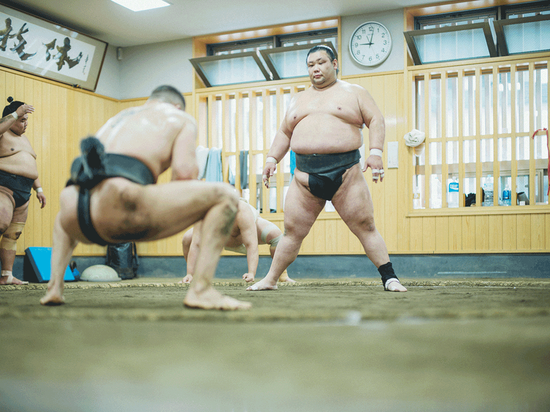 力士たちが、鳴戸部屋の稽古場でぶつかり稽古をしている。