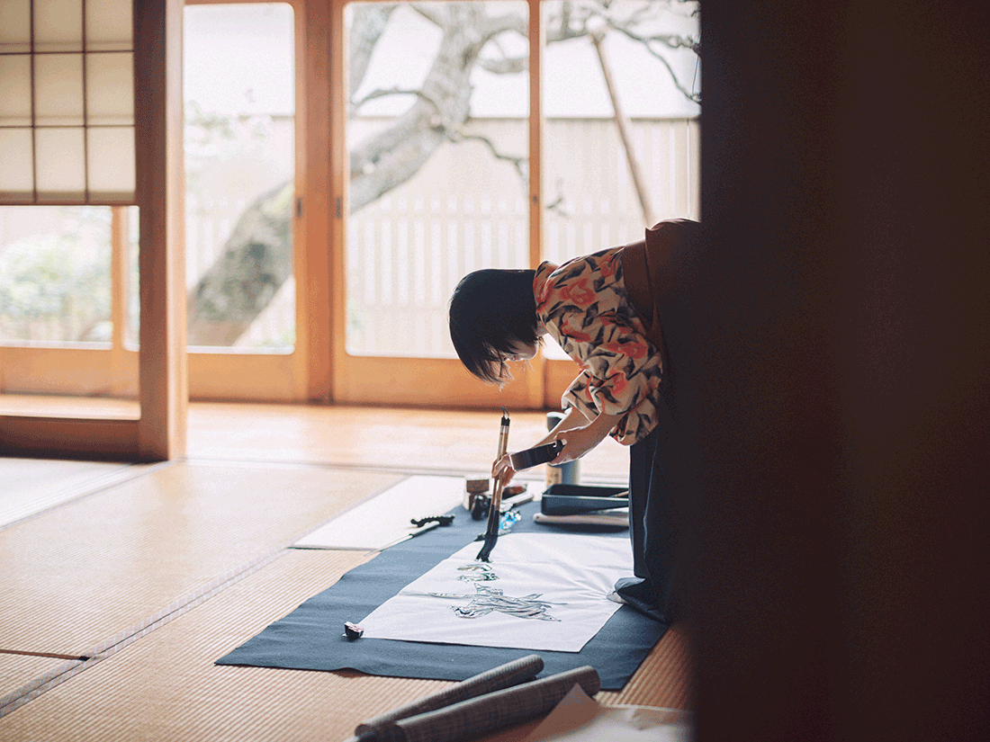 畳の部屋で書を書く女性の作業風景。
