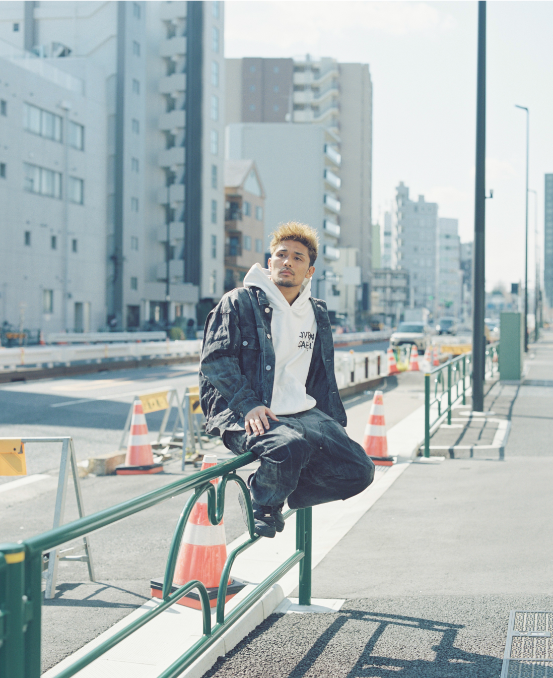 街中のガードレールに腰をかけている男性。