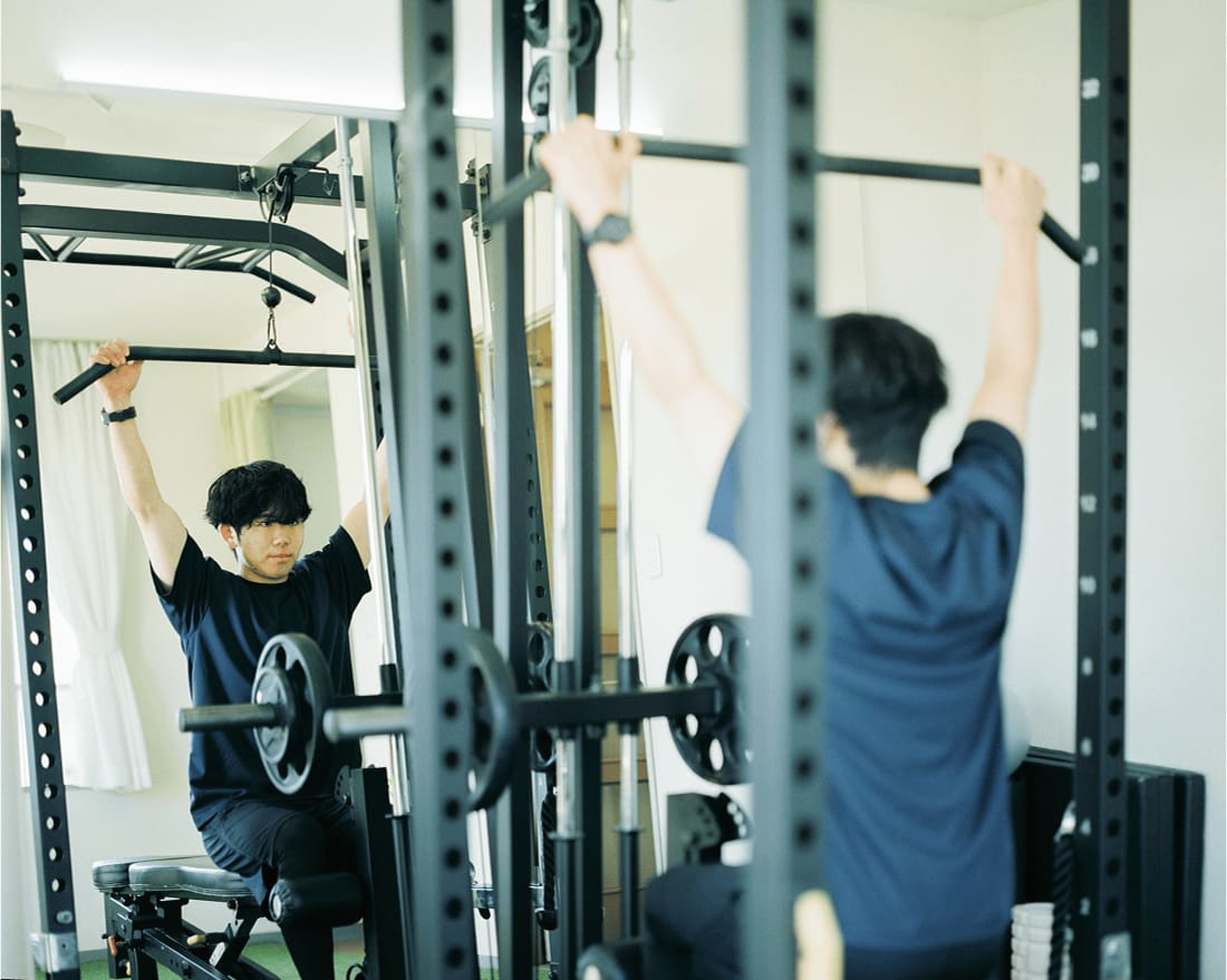 ジムでトレーニングに取り組む男性。鏡に映る自分のフォームを確認している。