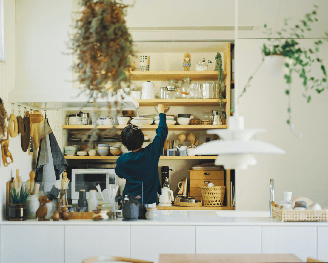 様々な食器が収納されている大きめの棚に手を伸ばす女性