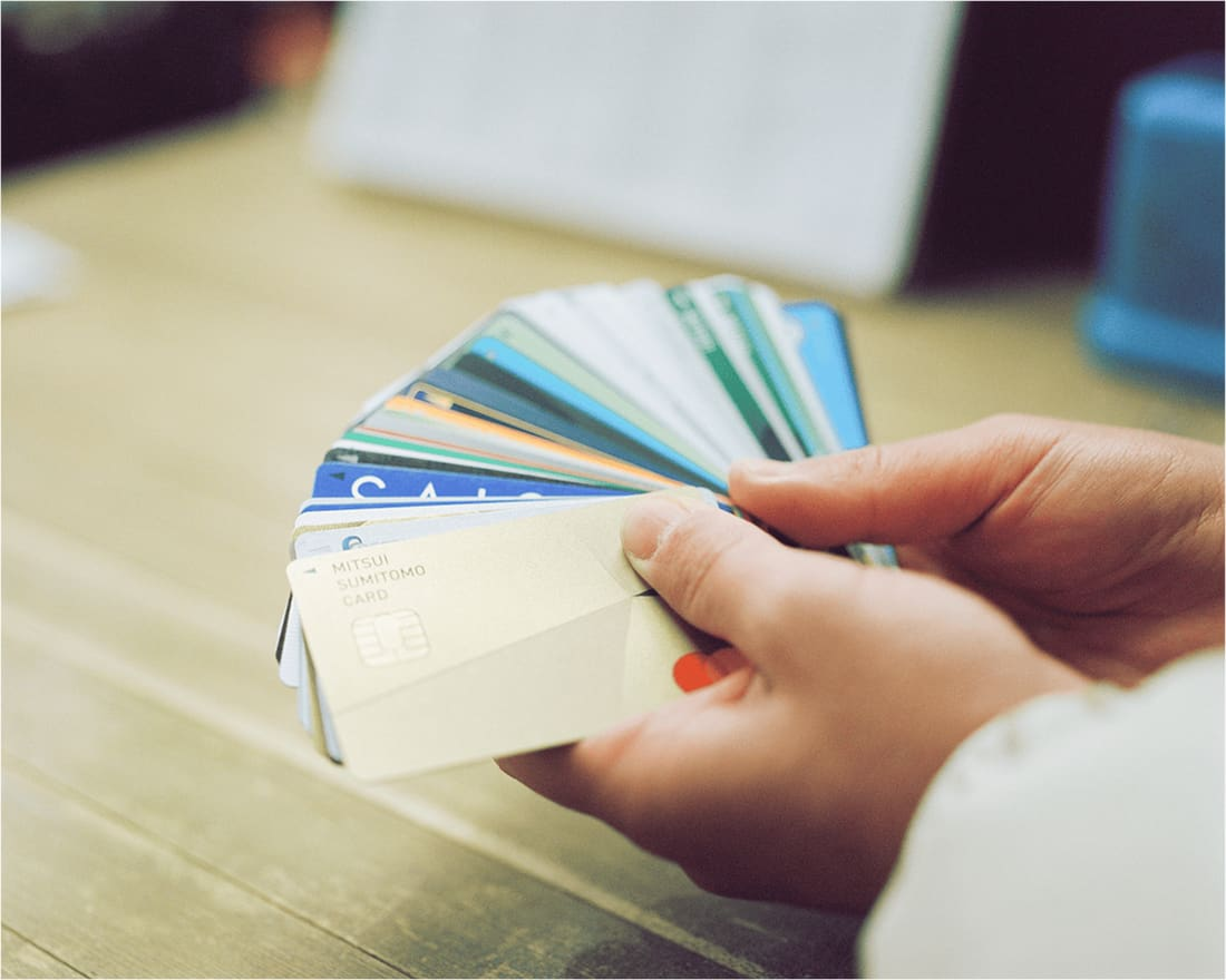 机の上で、色とりどりのクレジットカードを扇状に広げる男性の手元。
