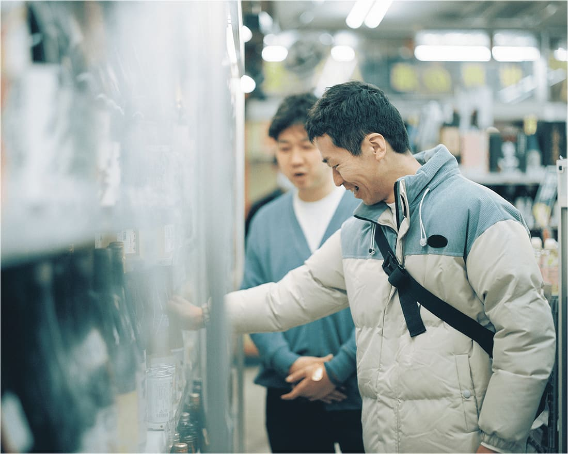 酒屋の店内で友人と談笑しながら商品を手に取る男性。和やかな雰囲気が漂う。