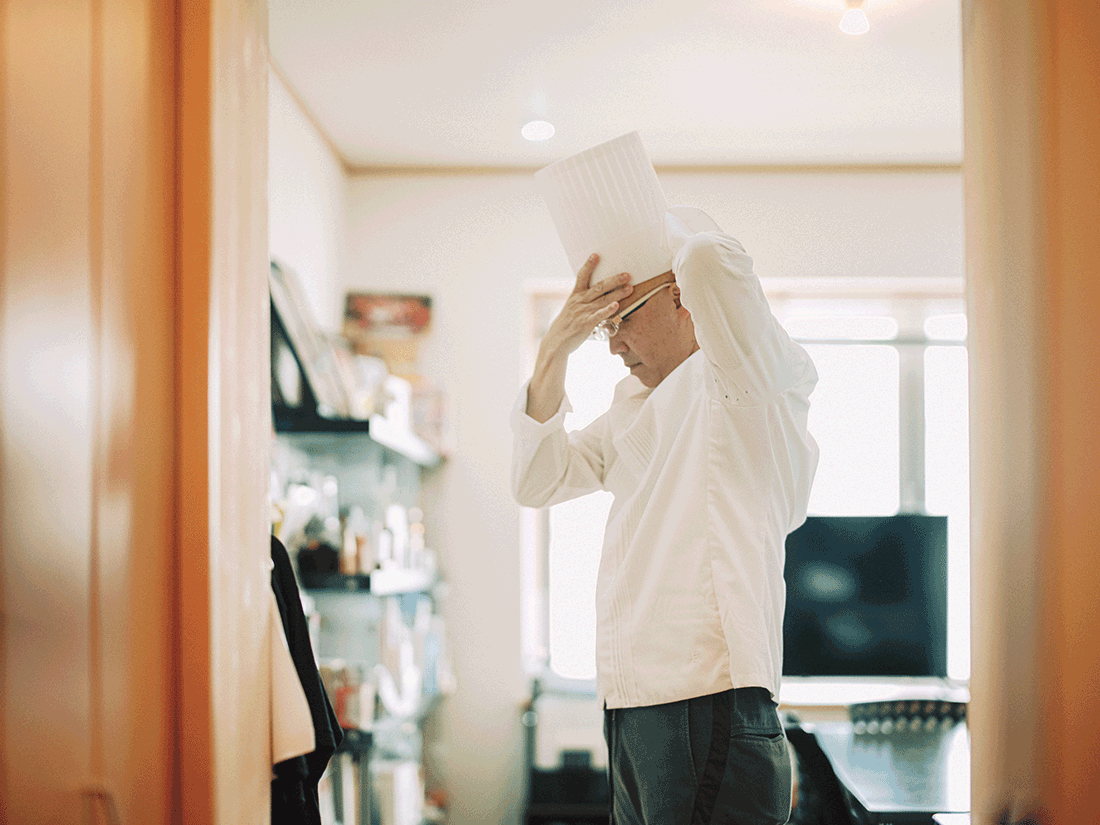 パティシエ・辻󠄀口博啓さんが、厨房でコック帽を身につけている。