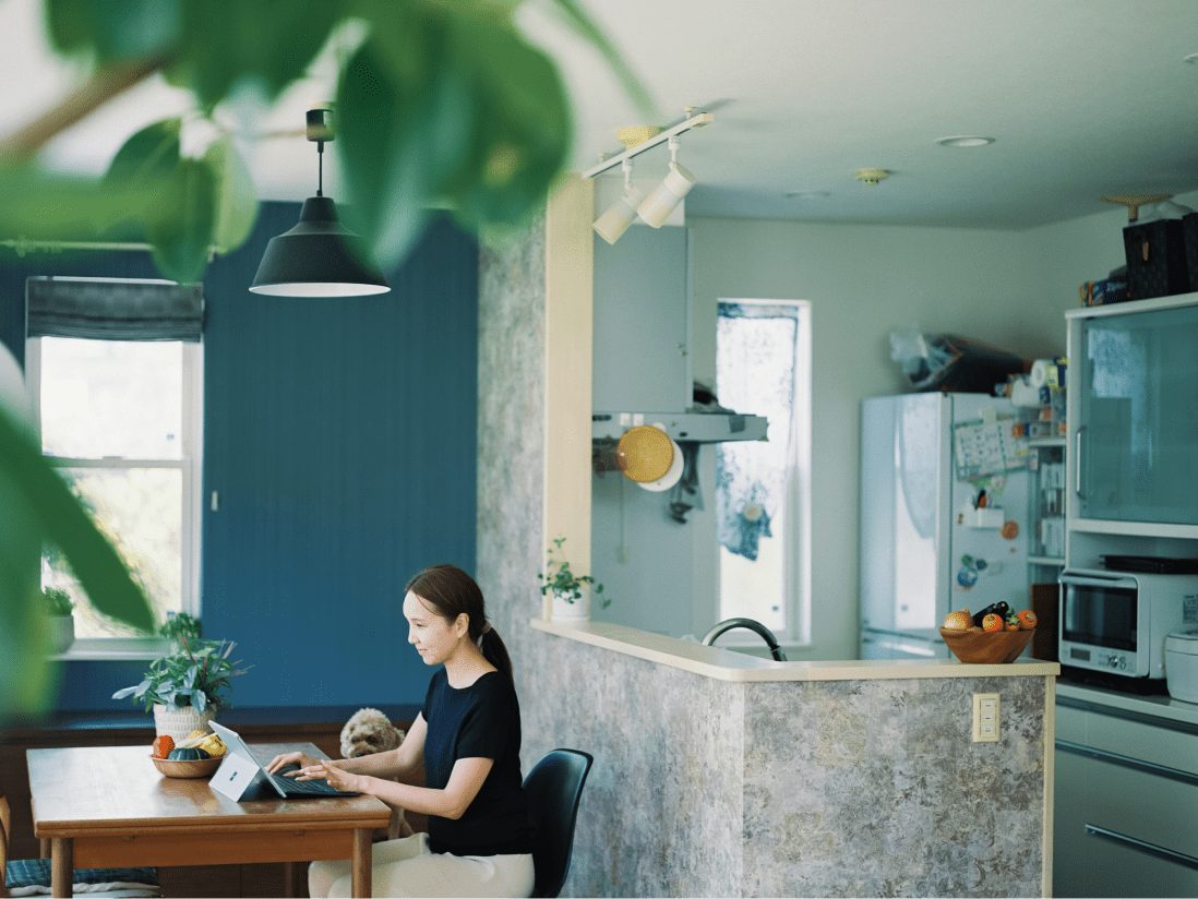 ダイニングにあるテーブルでパソコンに向かう女性と隣には愛犬。