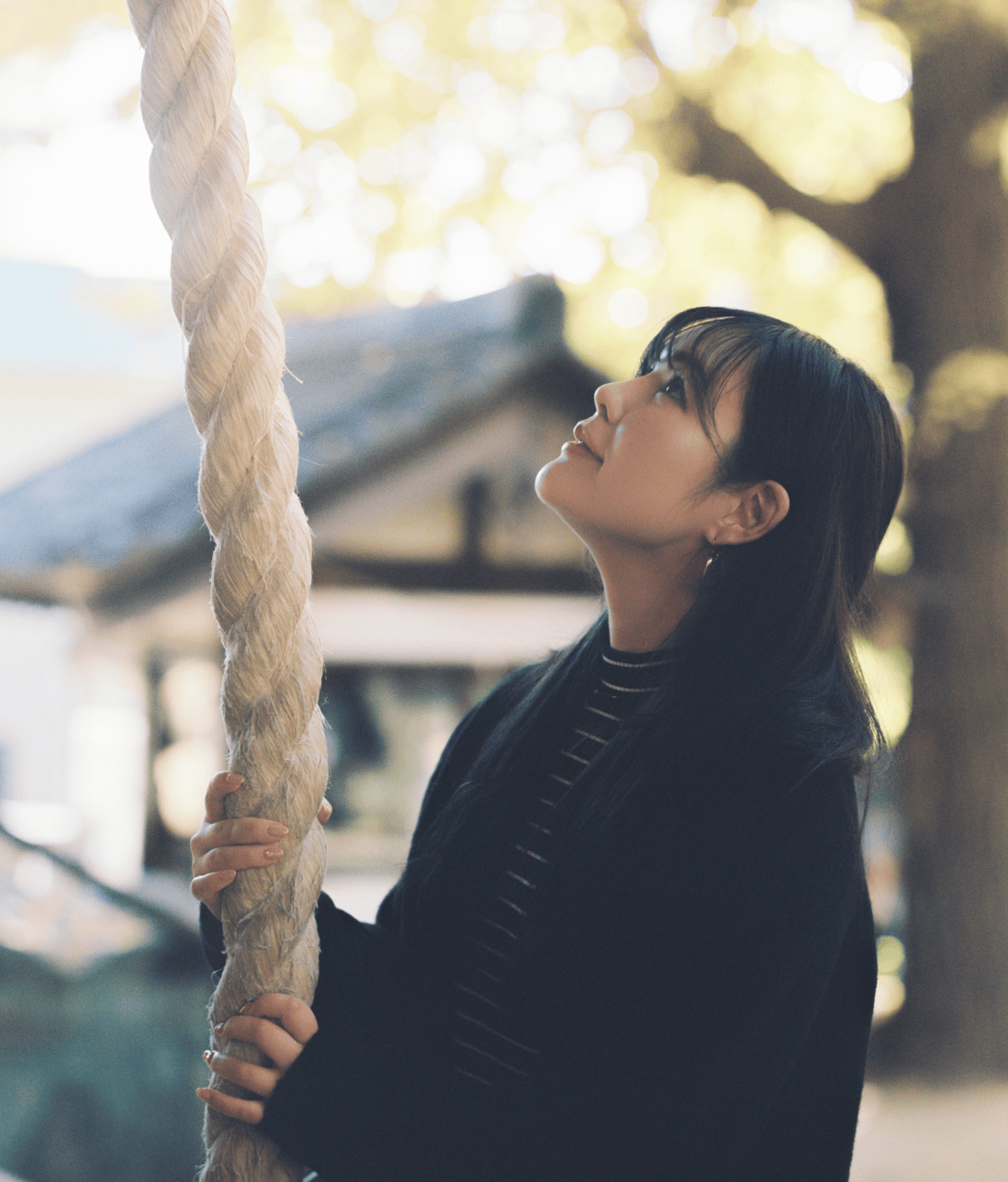 鈴緒の上を見つめている女性。