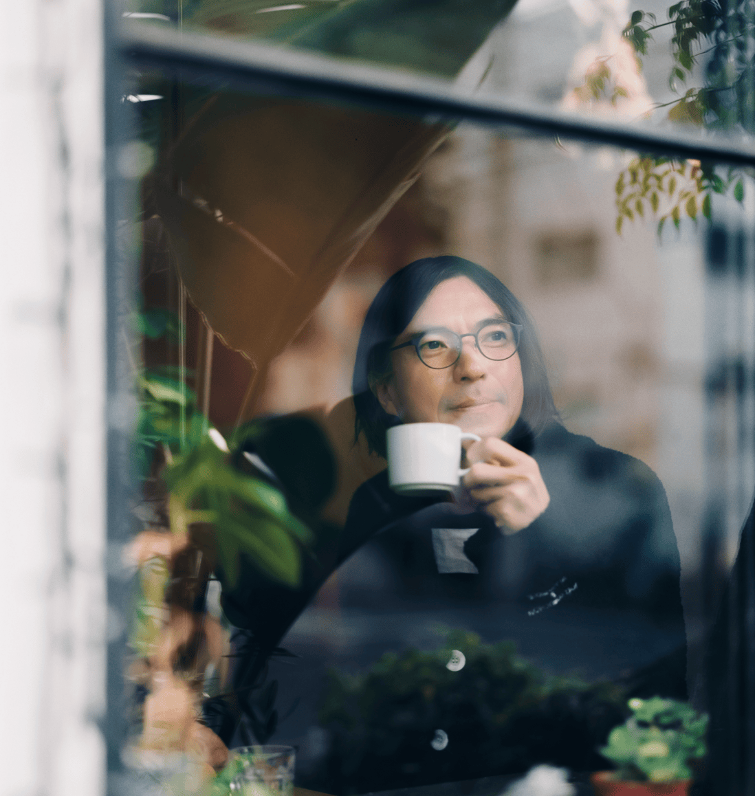 カップ片手に窓から外の様子を見ている男性。