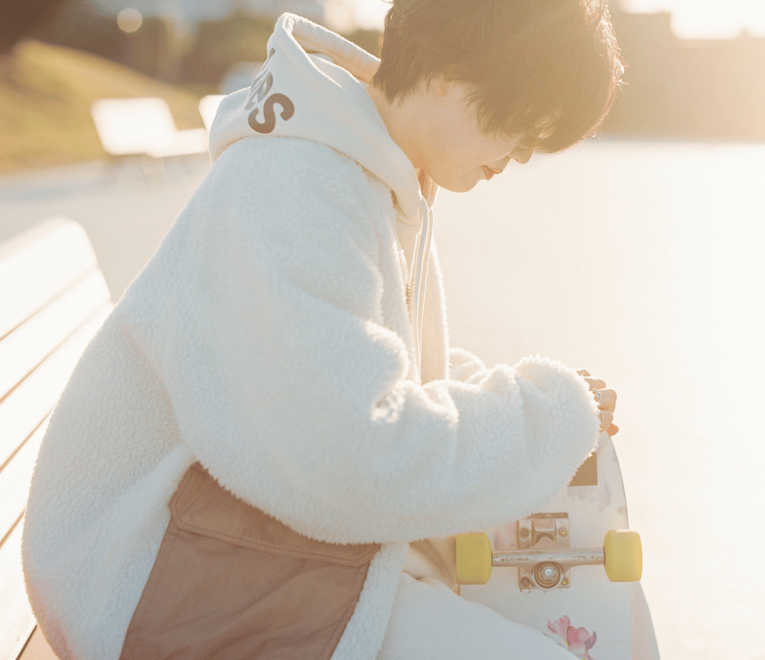 ベンチに腰をかけスケートボードに目を向けている様子